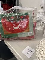 Photo of red Christmas tree skirt with white reindeer and snowflake patterns, in plastic packaging labeled 'White Reindeer Tree Skirt'