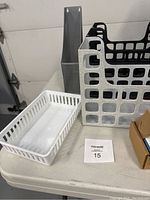 Desk organizers including black plastic file holders, a grey mesh organizer, and a white plastic tray arranged on a white table against a wall.