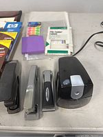 Photo of staplers and pencil sharpener, file folder labels, colored dot stickers, and sticky notes on table