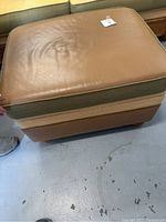 Top view of the brown leather padded cushion of the ottoman showing creases and some wear.
