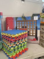 Photo showing stacked multi-colored foam rubber mats and a large wooden Connect 4 game
