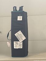 Photo of the folded and upright O Kids Pack and Play showing attached labels and dark fabric sides.