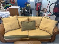 Front view of rattan framed sofa with beige back cushions and green seat cushions plus decorative pillows.