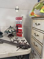 Photo showing fire extinguisher bracket box, stained glass ceiling lamp, and metal curtain rods on table
