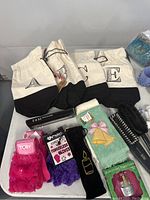 Photo showing new fingerless gloves in pink and purple with tags, mini bag, hair brushes, and green patterned socks with holiday design.