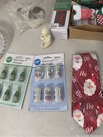 Photo showing glass oval dish, small snow baby figurine, Wilton brand champagne bottle and beer can shaped candles, and boxed Christmas items including fabric napkins with Santa faces.