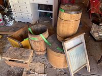 Overview of vintage barrels, crate, bench, washboard grouped together on floor.