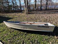 Side view of Grumman aluminum boat on grass, logo and hull condition visible