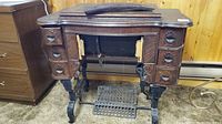 Front view of antique White treadle sewing machine cabinet with closed top showing wood grain and ornate black iron legs with foot pedal.