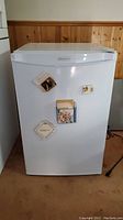 Front view of white Danby Simplicity SCR412W bar fridge with magnetic decorations on door