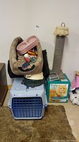 Overview photo showing cat scratching post, cat carrier, pink feeding bowls atop leopard print cat bed with various cat toys.