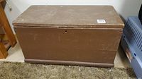 Front view of rectangular brown wooden chest with visible wear and scratches.