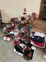 Overview of large collection of Christmas decorations and clothing on floor and containers