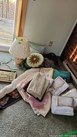 Overall view of the lot with cushions, curtains, tablecloths, embroidered wall art, and a table lamp placed on the floor.
