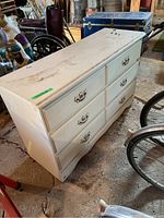 Side angled view showing six drawers with decorative handles, white paint, dirt marks on top.