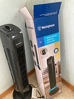 Black Westinghouse vertical oscillating electric heater next to original box, showing front and overall length.