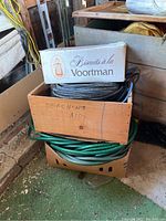 Cardboard and wooden boxes containing coiled garden hoses, extension cords, and rope in storage.