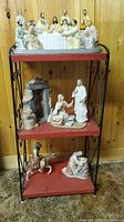 Full view of three-tier shelf with multiple religious figurines including Last Supper set on top, Jesus with woman kneeling on middle shelf, and person on donkey and kneeling woman on bottom shelf