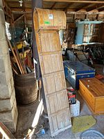 Full view of the wooden toboggan standing upright against a stove, showing length and curved front.