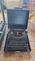 Front view of black Remington Rand Deluxe Model 5 typewriter inside its case with lid open showing keys and type basket.