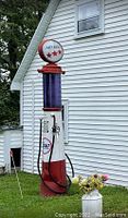 Full view of red and white metal gas pump with purple glass cylinder and illuminated globe