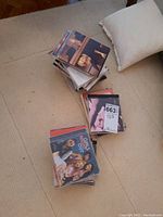 Photo of stacked CDs on beige carpet with pillow visible, showing assorted music CD cases with visible covers including Girls Night Out.