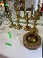 Four brass candlesticks and one brass ashtray arranged on a table with labels showing sizes and lot number.