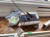 The ceiling lift control motor unit with attached electrical cords and control handset beside a bag of mounting accessories and track rail.