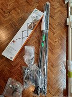 Photo showing metal curtain rods bundled and wrapped in plastic, with parts and mounting hardware visible, and unopened drying rack box.