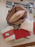 Top view of a white bag filled with beige and tan decorative cushions. Several cushions and covers including a red quilted one and a cream-red striped one are visible outside the bag.