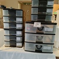 Front view of four stacked plastic box organizers with labeled drawers such as 'Hardware for Home','Paint Set 3 drawers', 'Workers Cables', 'Scissors Marks Brass 2' and others.