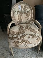 Front view of one carved wood armchair showing oval back and leaf-patterned upholstery