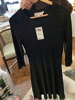 Black knit dress held on a hanger, showing full length and ribbed texture.