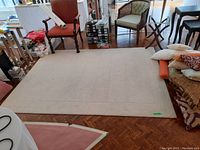 Full view of light beige IKEA area rug on wooden floor, showing scale with nearby chairs and pillows