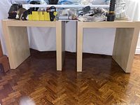Two light wood side tables with various items on top (items not included). Tables have simple modern design with straight leg supports and flat rectangular surfaces.
