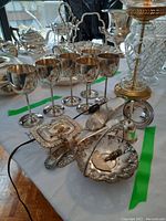 Full view of the silver plate wine cups, candy dish, scoops, bell, and serving utensils on a table.