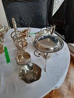 Photo showing silver plate teapot missing knob, wine bottle holder, small bowl and some servers on a round table