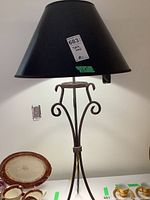 Full view of the table lamp showing the black conical lampshade and metal curved base design alongside some china dishes.