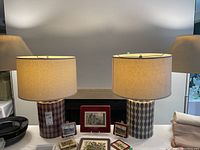 Full view of two matching ceramic table lamps with beige drum shades, showing geometric pattern on lamp bases.