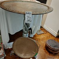 View showing the decorative metal tray table top on the twisted leg wood stand and the round metal basket below, along with two wooden plant bases on the floor.