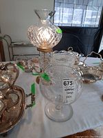 Photo showing Waterford glass lamp with cut glass chimney and base alongside etched glass vases and other silver pieces on a table