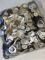 Bag filled with a large collection of various sizes and colors of hand-carved abalone and mother of pearl buttons.