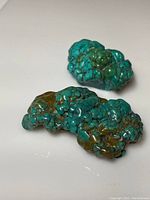 Two large turquoise boulders lying on a white surface, showing surface textures and matrix patterns.