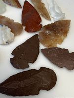 Close-up view of multiple arrowheads on a white background showing flaked surfaces and color variations.