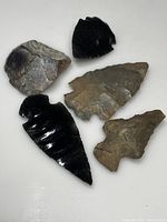 Five assorted indigenous arrowheads and stone fragments on white background