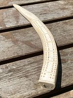 Photo showing the full curved cribbage board with carved rectangular holes for scoring resembling domino dots. The bone or ivory material is visible with natural color variations and surface wear.