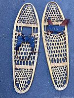 Top view of pair of Inuit made snow shoes showing wooden frame, woven webbing and leather bindings with buckles.