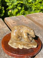Front and side view of Inuit soapstone bear sculpture on wooden stand placed on wooden surface outdoors.