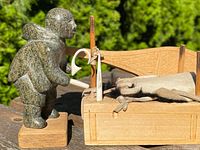 Close side view of the soapstone Eskimo figure holding a wooden staff next to the wooden dog sled with soapstone dogs visible.