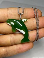 Front view of carved green jade and marble killer whale orca pendant with sterling silver chain, held in hand showing size and detail.